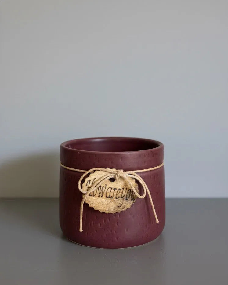Maroon ceramic cup with a string label on a gray surface and light gray background