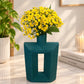 A teal geometric ceramic vase with a hollow center, filled with a bouquet of bright yellow daisy-like flowers, set on a light marble countertop in a styled interior scene.