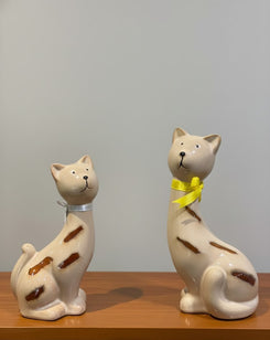 Two ceramic cat figurines on a wooden surface with a plain background